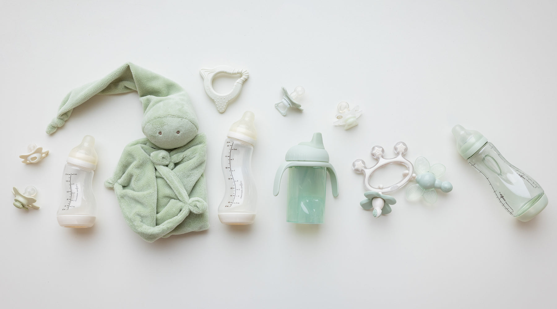 Difrax babyproducten collectie flatlay met blauwe babyflessen, fopspenen, houten speelgoed autootje en blokjes, hydrofiel doek, babykleding en verzorgingsproducten in zachte blauwe en naturel tinten