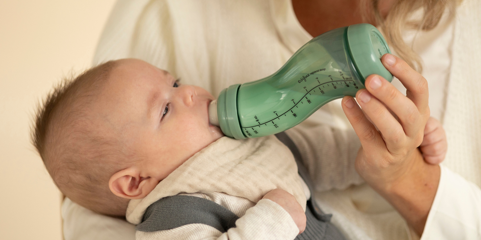 Baby die melk drinkt bij mama uit een groene babyfles