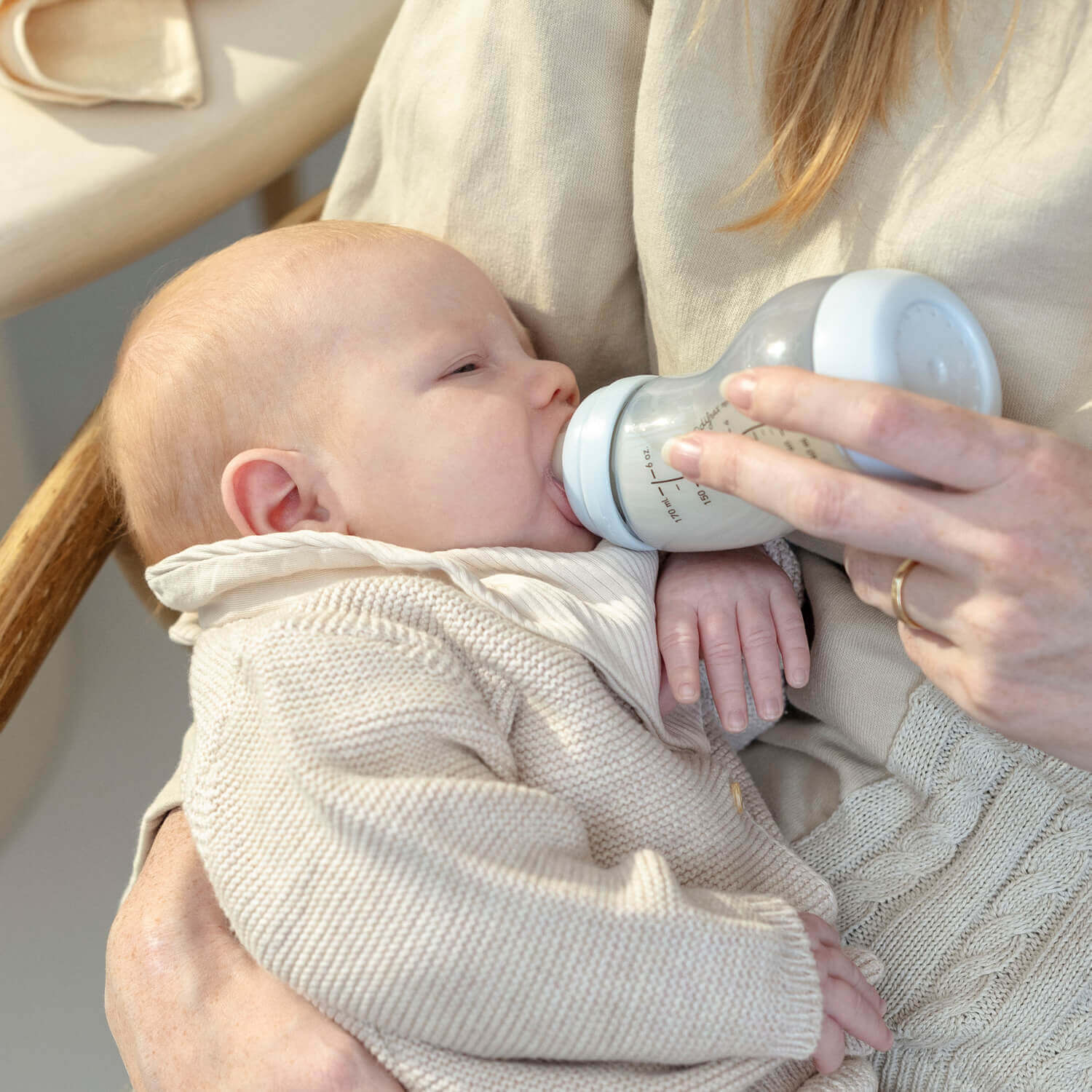 Moeder voedt pasgeboren baby met ijsblauwe Difrax S-fles in comfortabele voedingspositie, close-up van het voedingsmoment