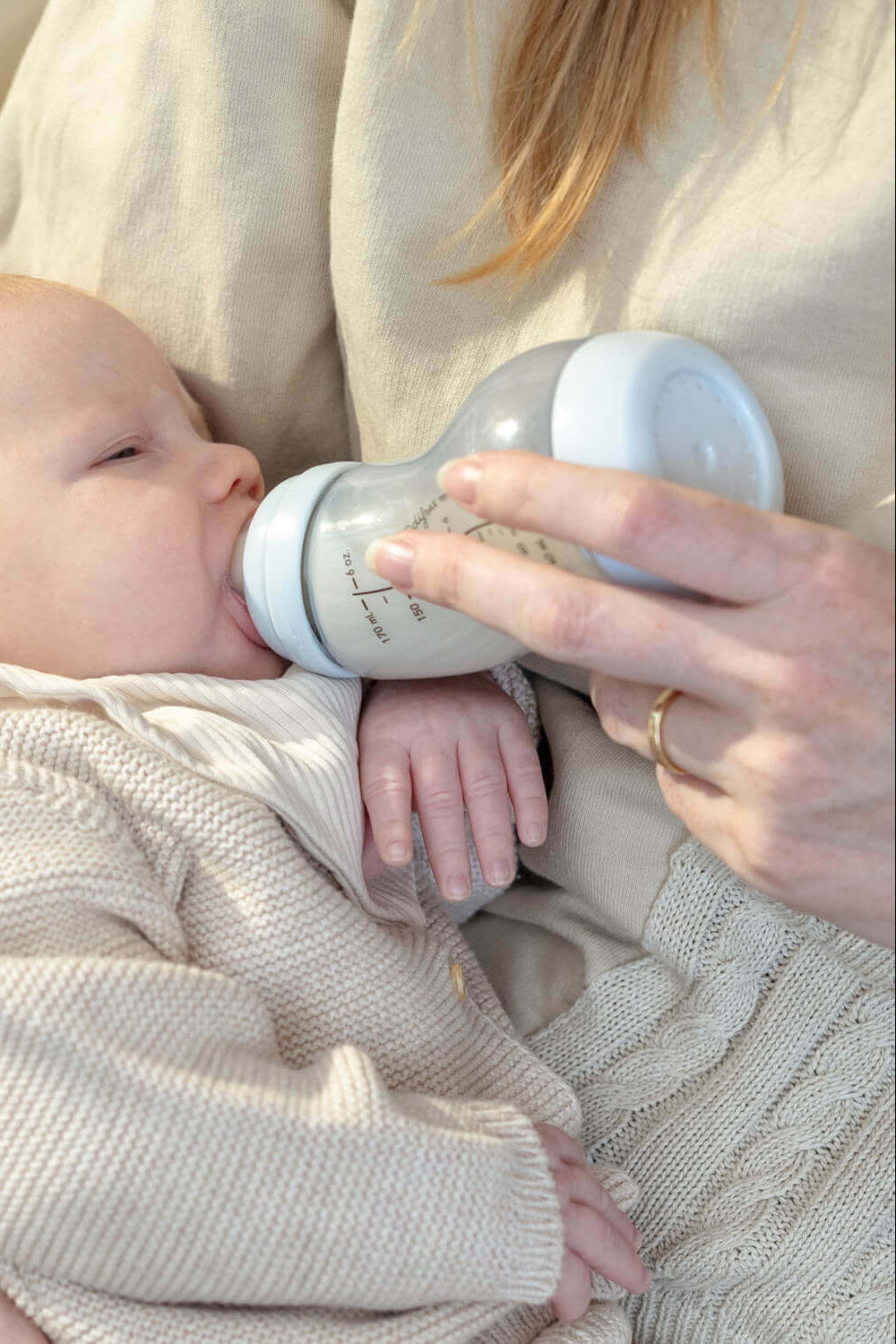 Moeder voedt pasgeboren baby met ijsblauwe Difrax S-fles in comfortabele voedingspositie, close-up van het voedingsmoment