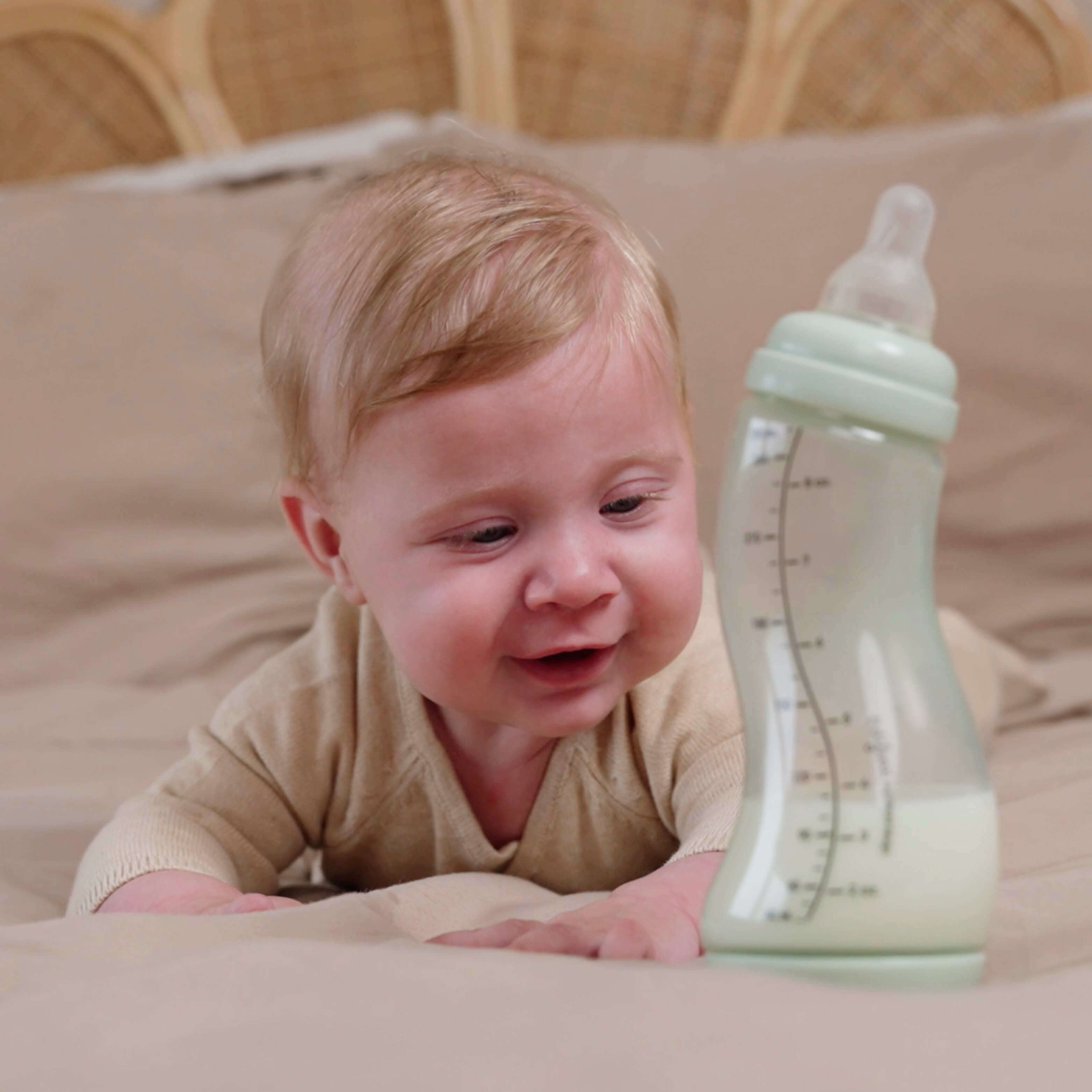 Lachende baby tijdens buikligtijd naast pistachgroene Difrax S-fles 250ml gevuld met moedermelk, speelse en vrolijke sfeer