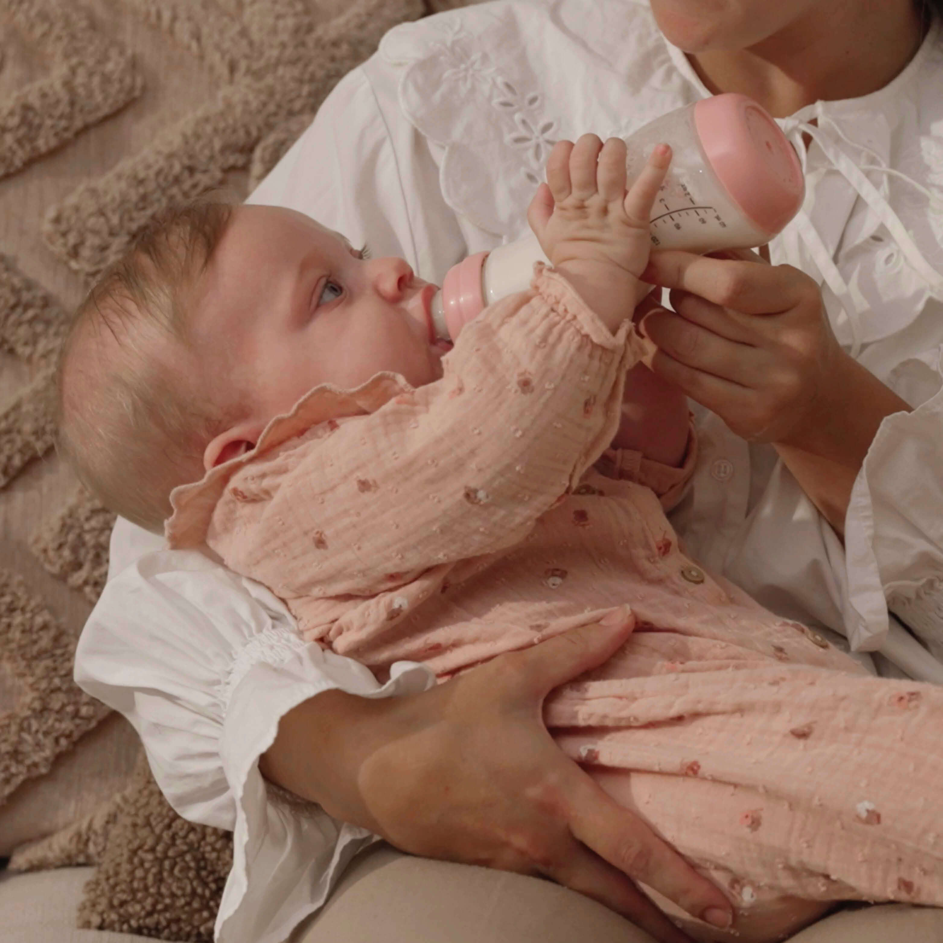 Baby in roze kleding wordt gevoed met Pink Opal Difrax S-fles 250ml, liefdevolle voedingssituatie op zachte ondergrond