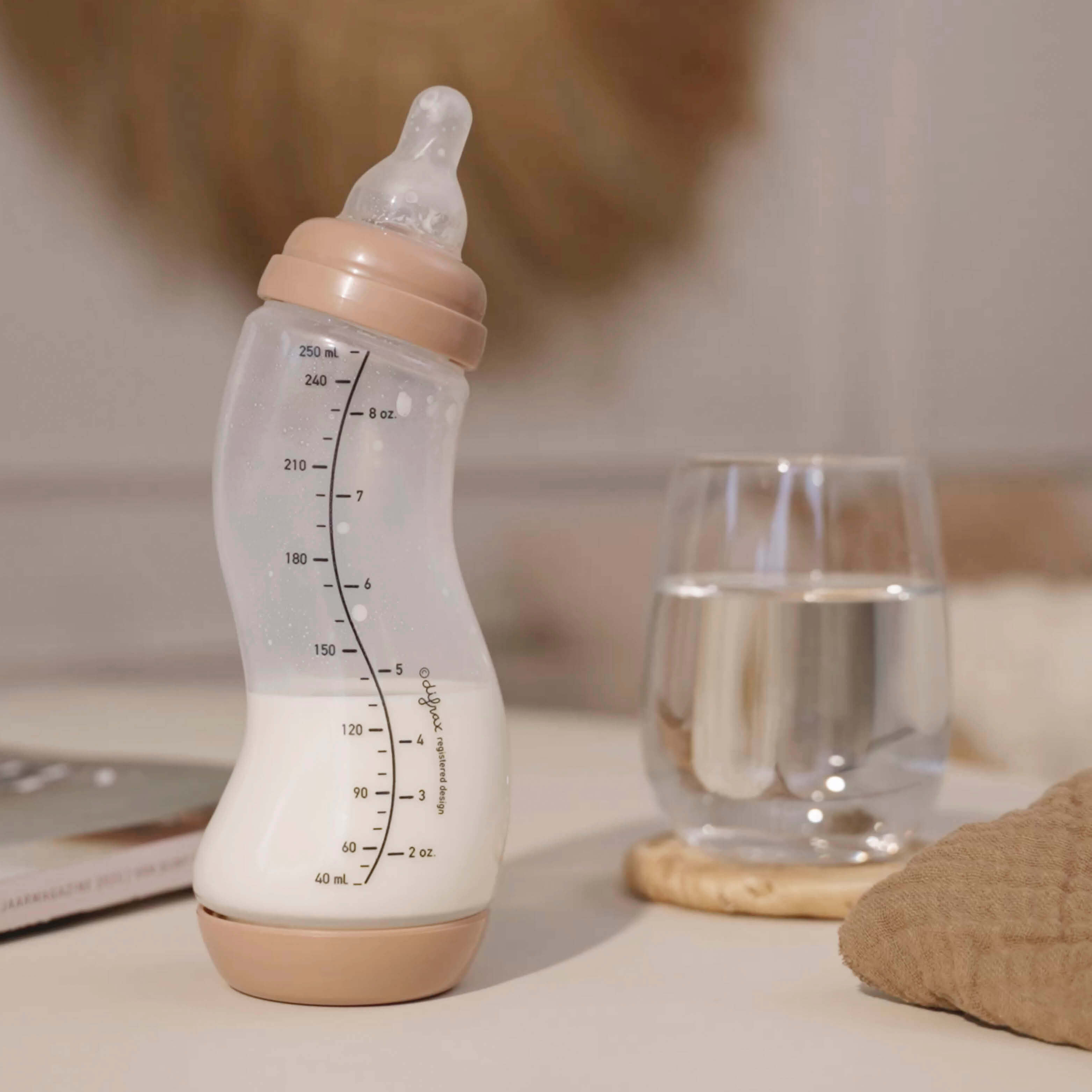 Mocha beige Difrax S-fles 250ml gevuld met moedermelk op tafel met waterglas, rustgevende lifestyle setting
