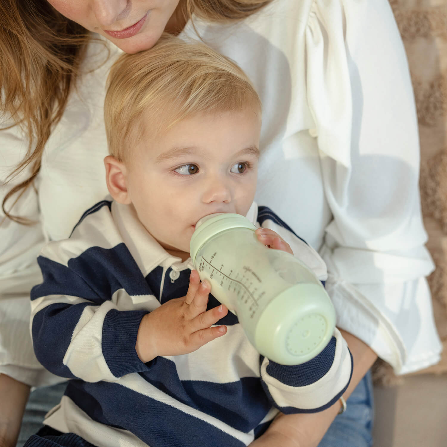 Peuter drinkt zelfstandig uit pistachgroene Difrax S-fles 310ml bij moeder, stimulering van zelfstandig drinken