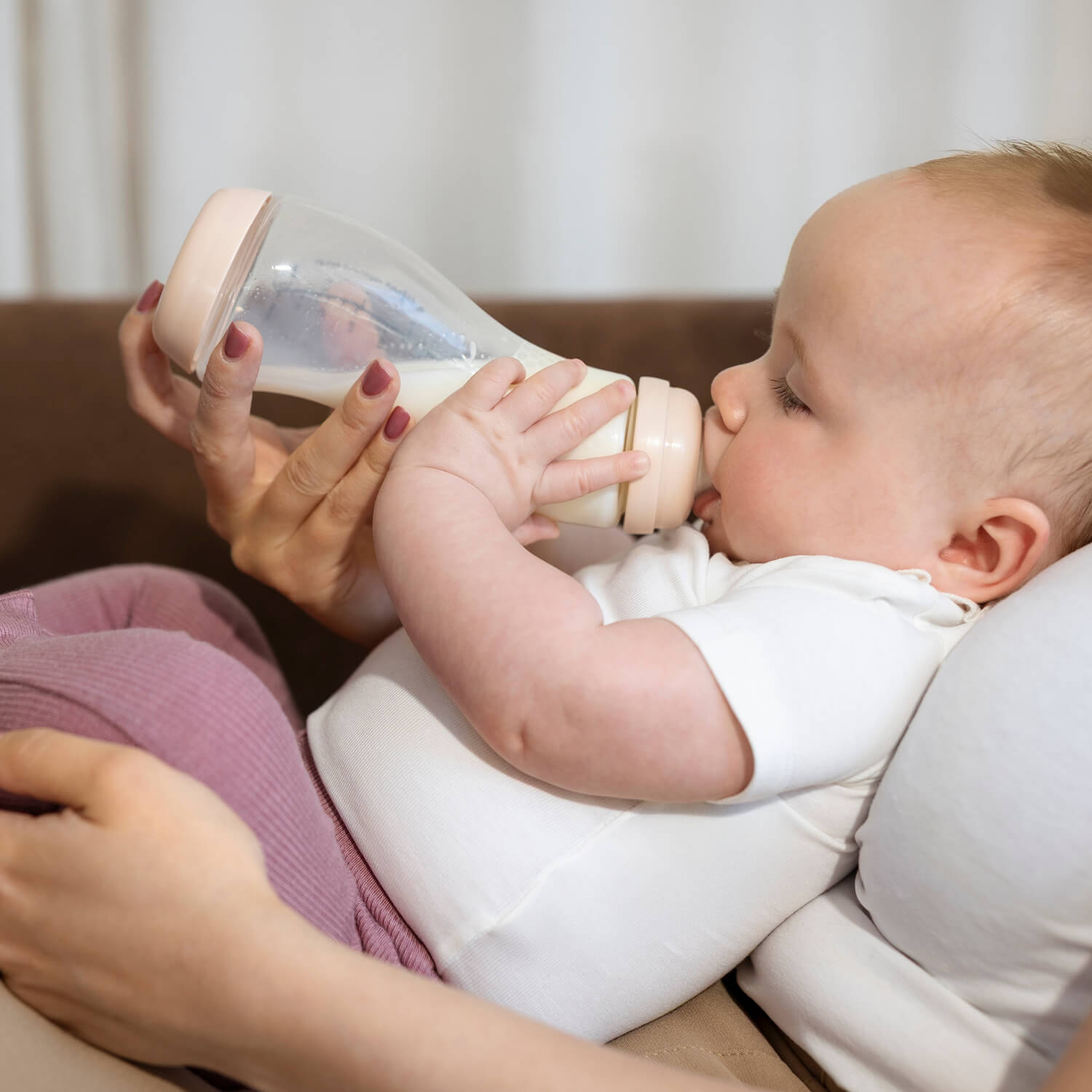 Baby drinkt uit Difrax glazen S-fles kleur Blossom (roze) terwijl moeder de fles vasthoudt – anti-colic glazen babyfles