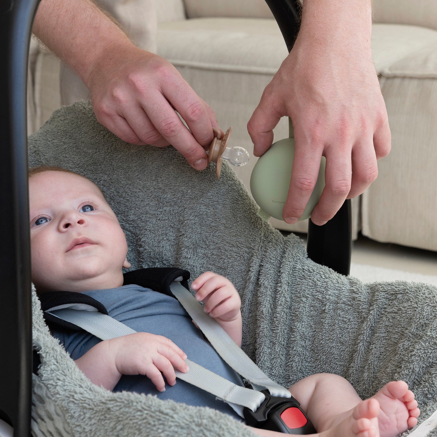 Un enfant est couché dans la poussette et le papa prend la sucette dans l'étui Difrax Lovi Silliconen.