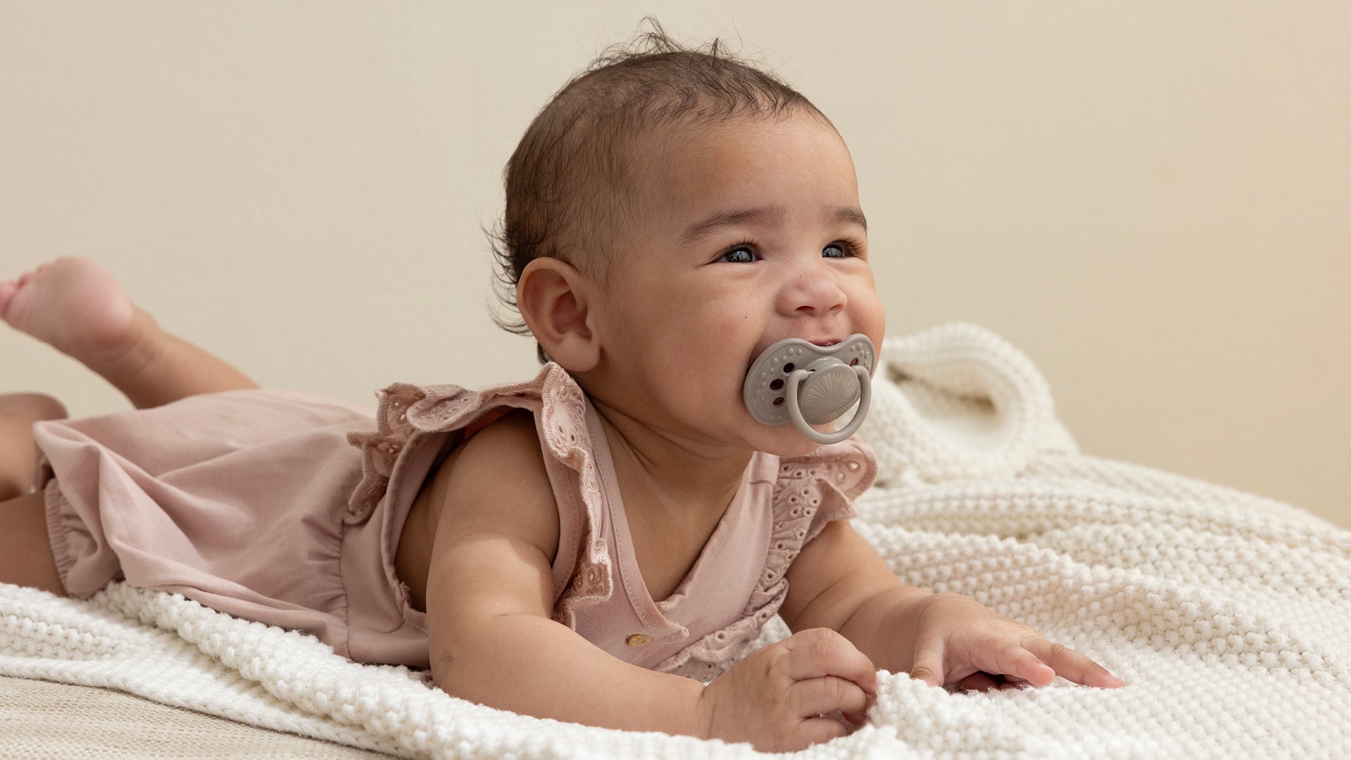 Un bébé de 6 mois est allongé sur le ventre avec un grand sourire. Elle a une sucette Difrax LOVI de la collection Harmony