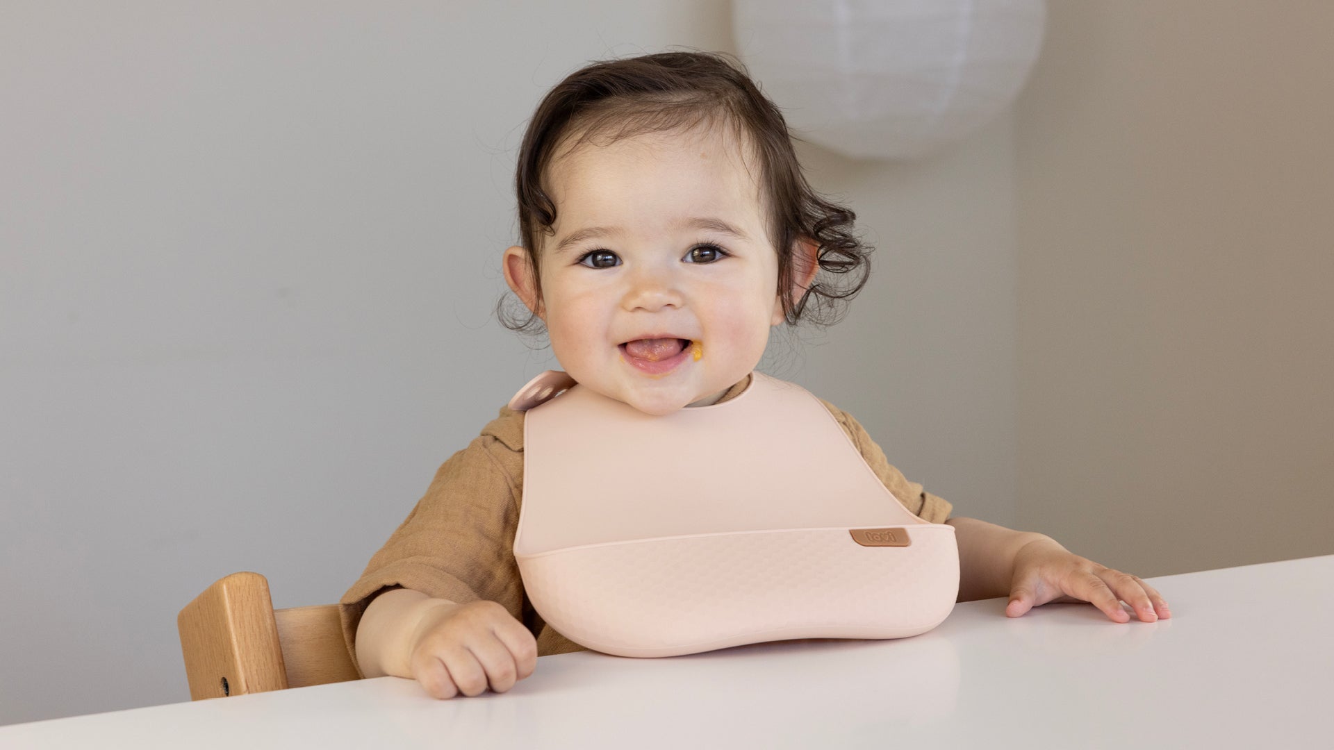 Un bambin heureux est assis à table et porte le bavoir en silicone.