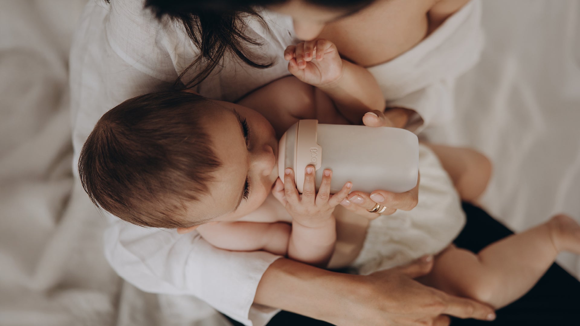 Le bébé est allongé dans les bras de sa maman et boit du lait d’un biberon Mammafeel