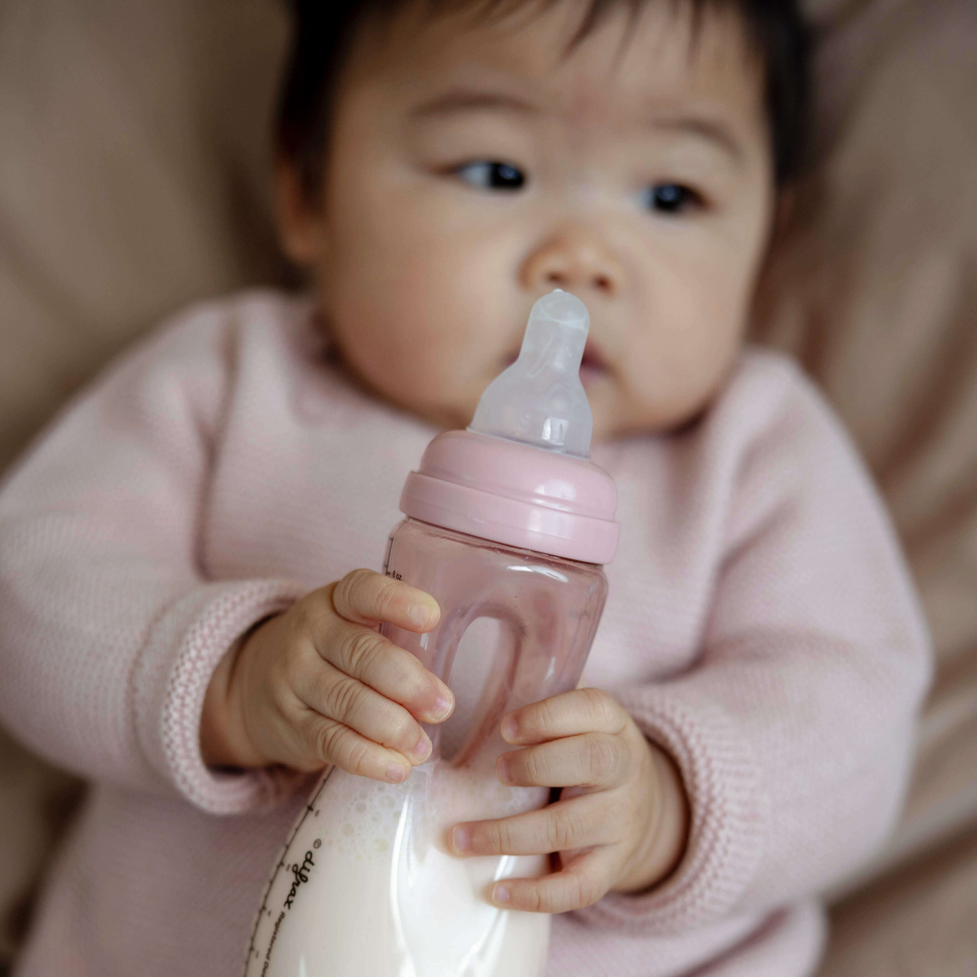 Baby in roze kleding houdt zelfstandig Pink Opal Difrax Easy Grip fles vast met beide handjes tijdens drinken