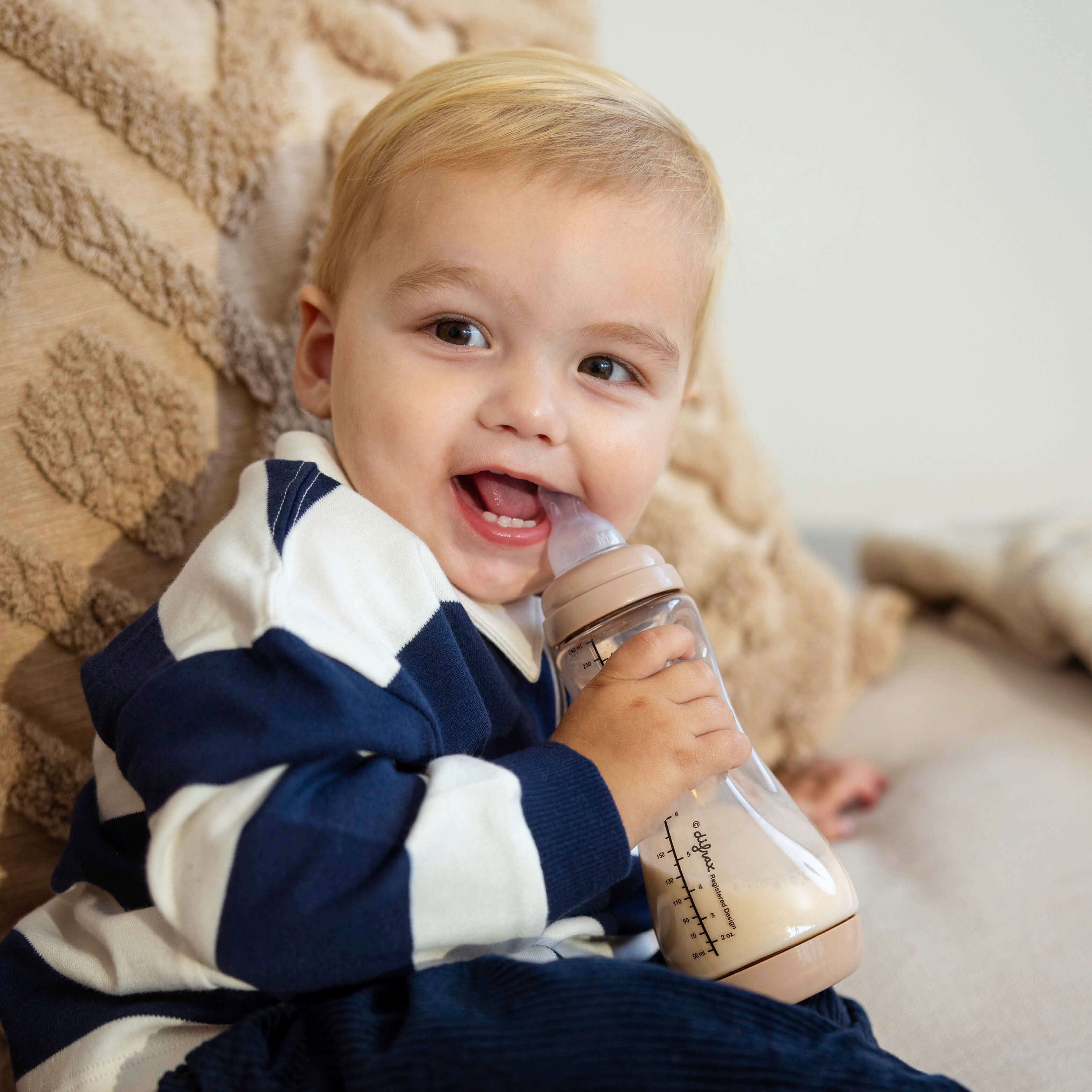 Lachend peuter kind drinkt zelfstandig uit Mocha beige Difrax Easy Grip fles, ontwikkeling van zelfstandigheid