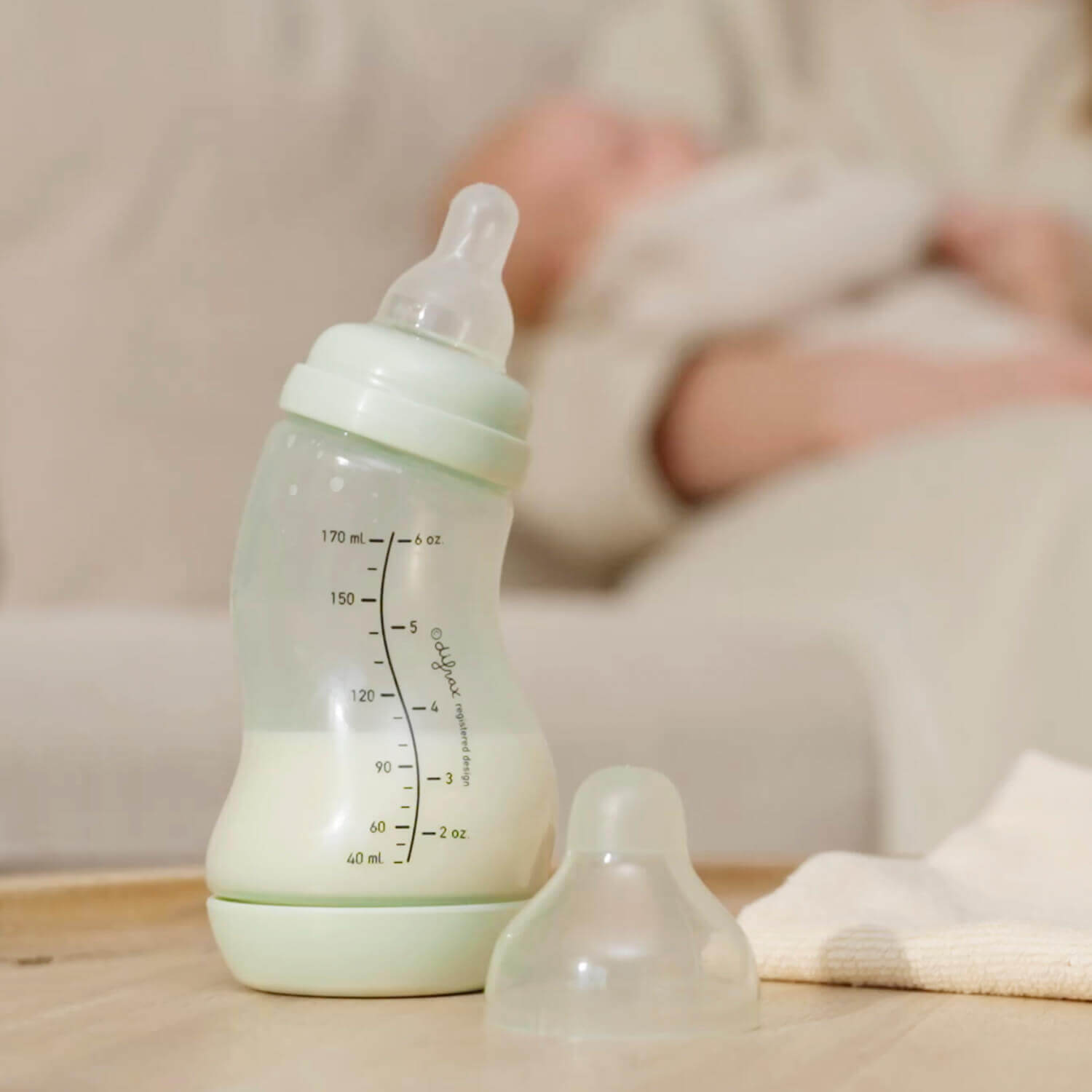 Pistachgroene Difrax S-fles met extra speen op voorgrond, slapende baby op de achtergrond, kalme voedingsomgeving
