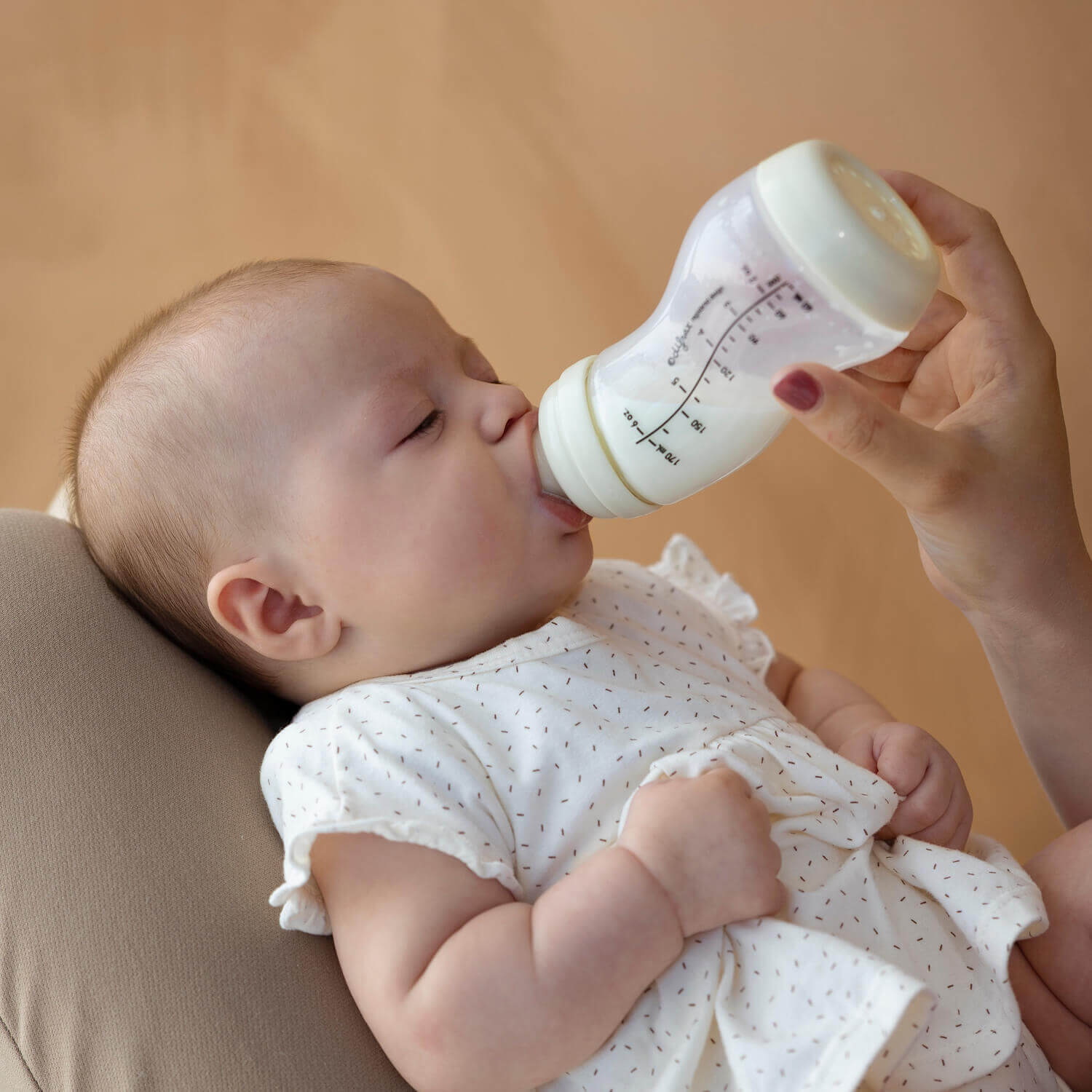 Baby wordt gevoed met ivoorkleurige Difrax S-fles, rustgevende setting met pasgeboren in wit kleding